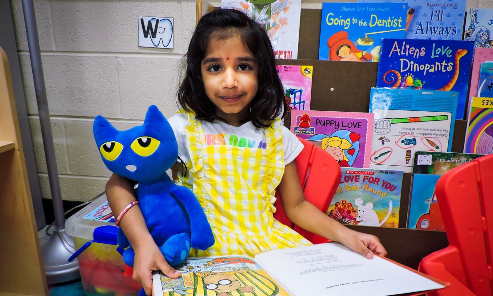 A girl smiles while reading a book and holding a toy